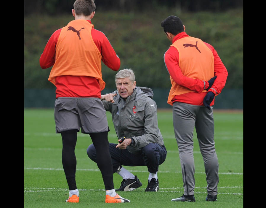 HLV Arsene Wenger ngồi xổm chỉ đạo các học trò. Ảnh: Express.